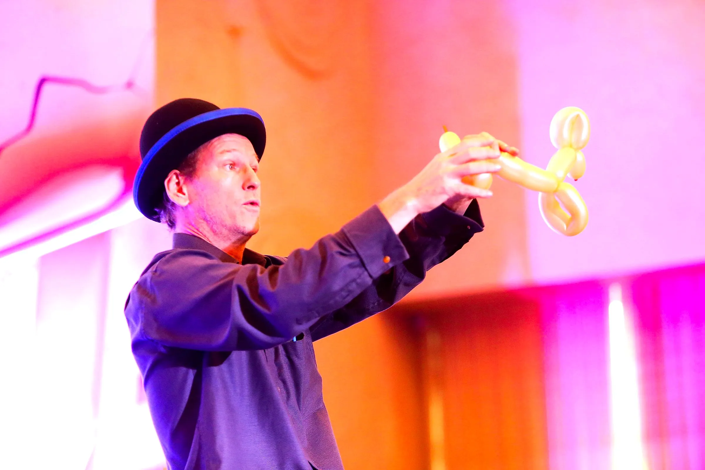 Balloon artist in a bowler hat holding up a balloon dog on stage
