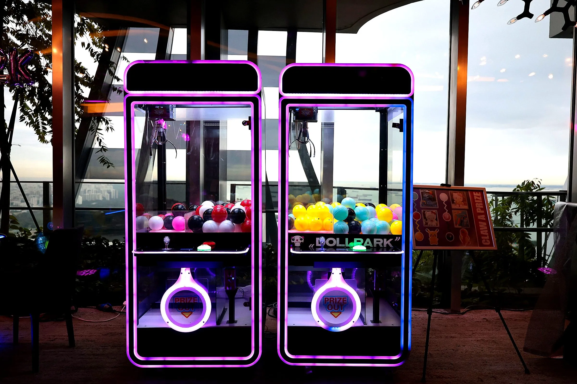 Two glowing claw machines filled with colourful prizes on a rooftop terrace