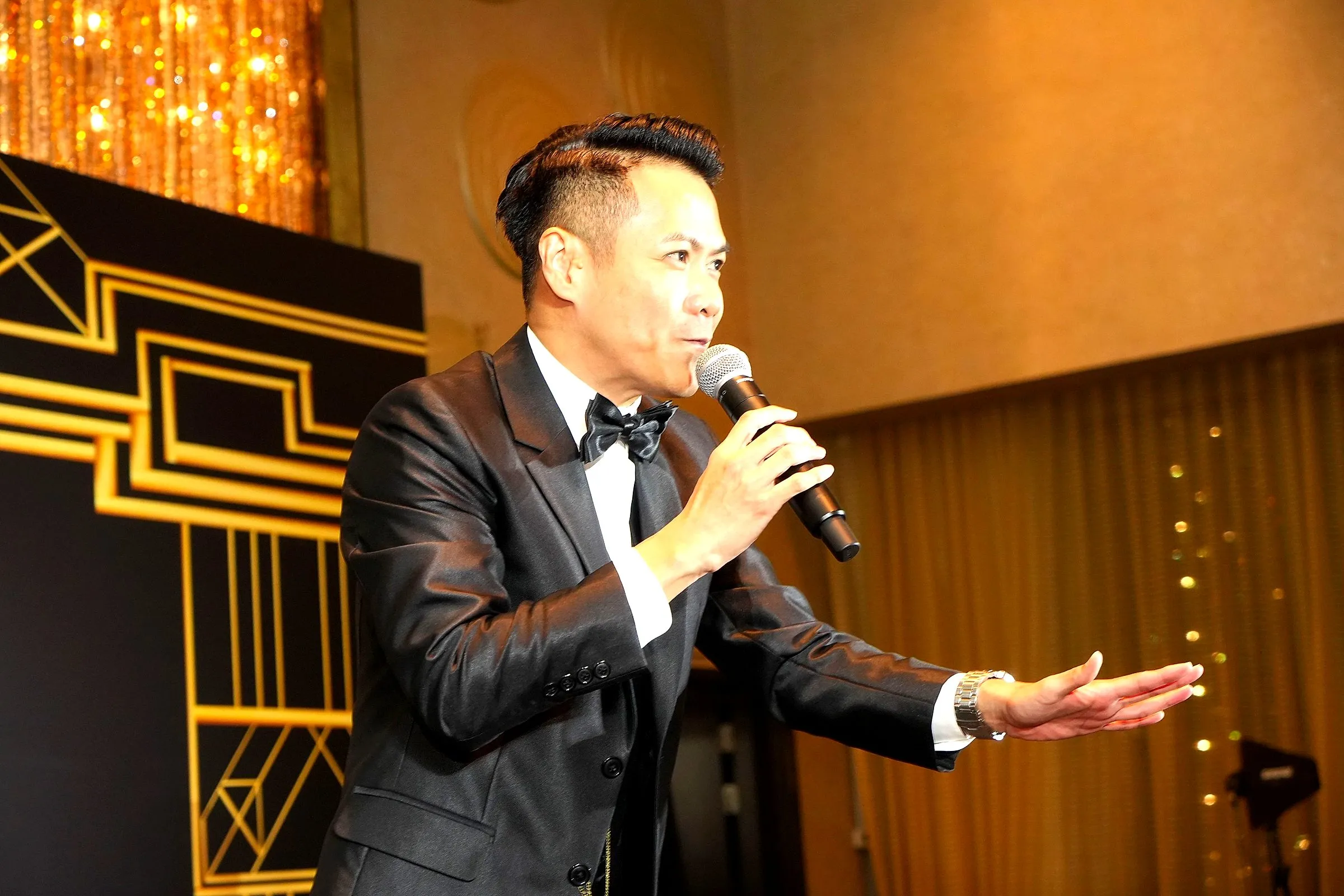 Host in a tuxedo addressing the room in front of a themed backdrop