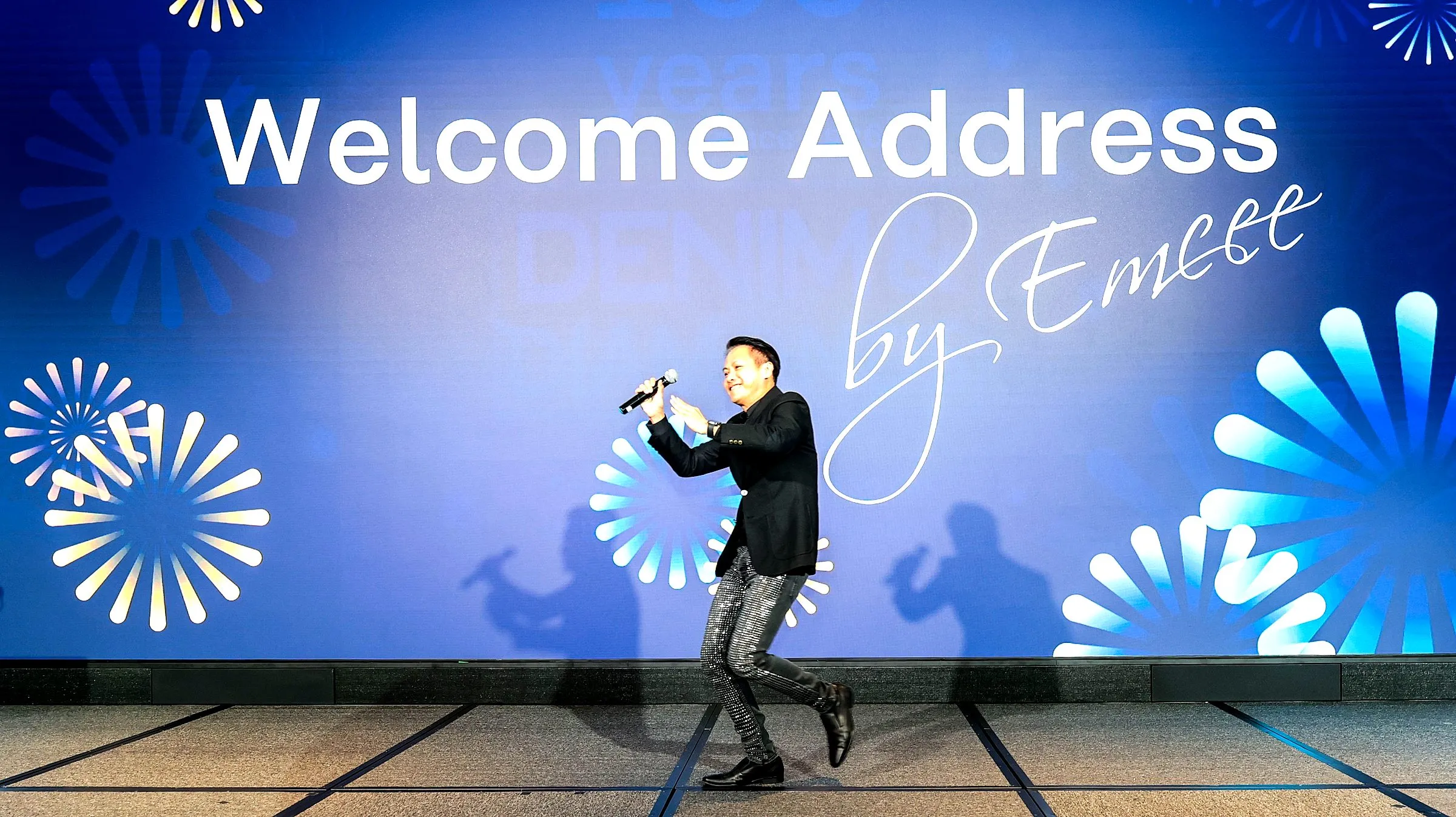 Emcee opening the evening on stage in front of a large welcome screen