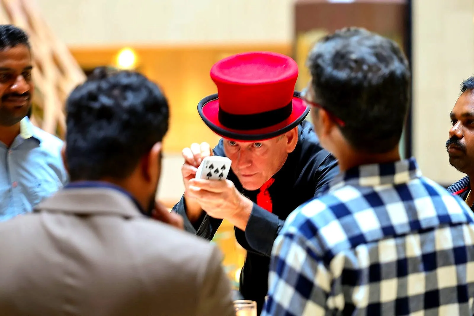 Magician in a red top hat performing a close-up trick for dinner guests