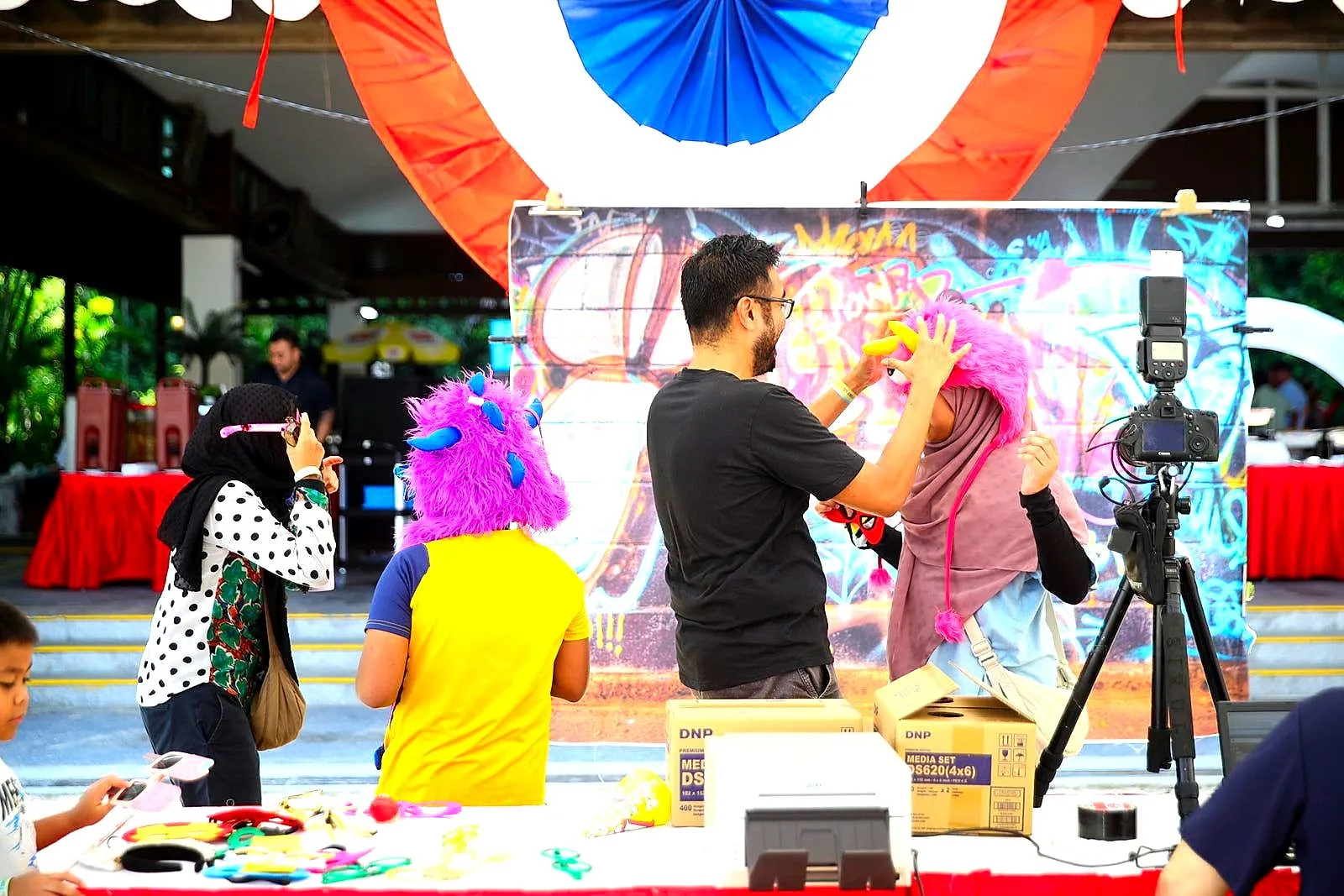 Guest in a bright wig and props beside a camera on a tripod