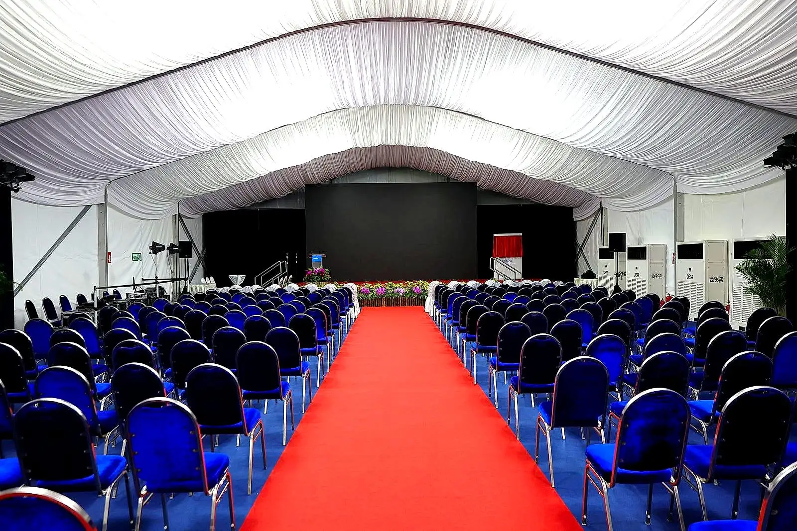 Red carpet aisle leading to a stage inside a large conference marquee