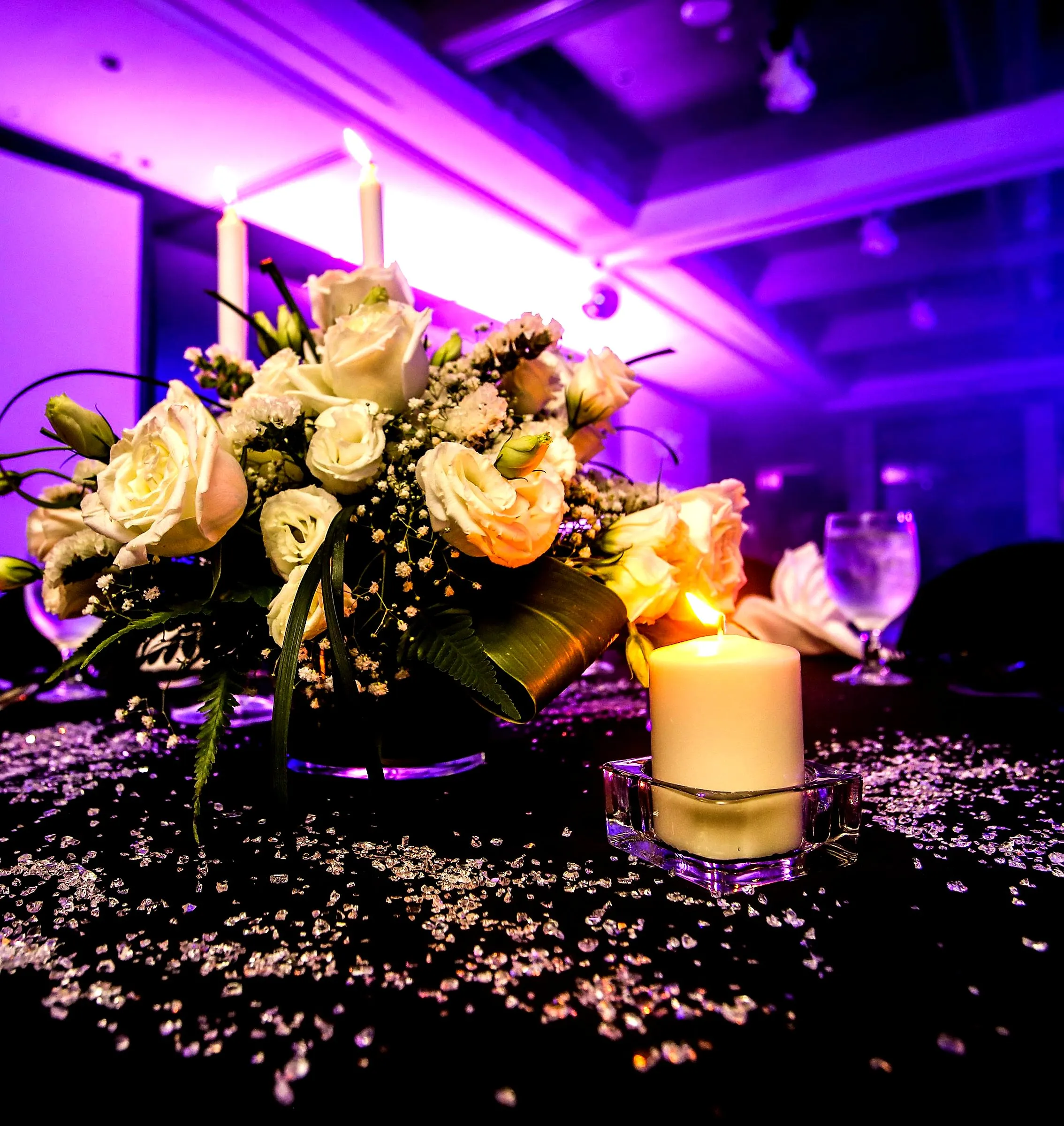 White rose and candle centrepiece on a dark table scattered with crystals